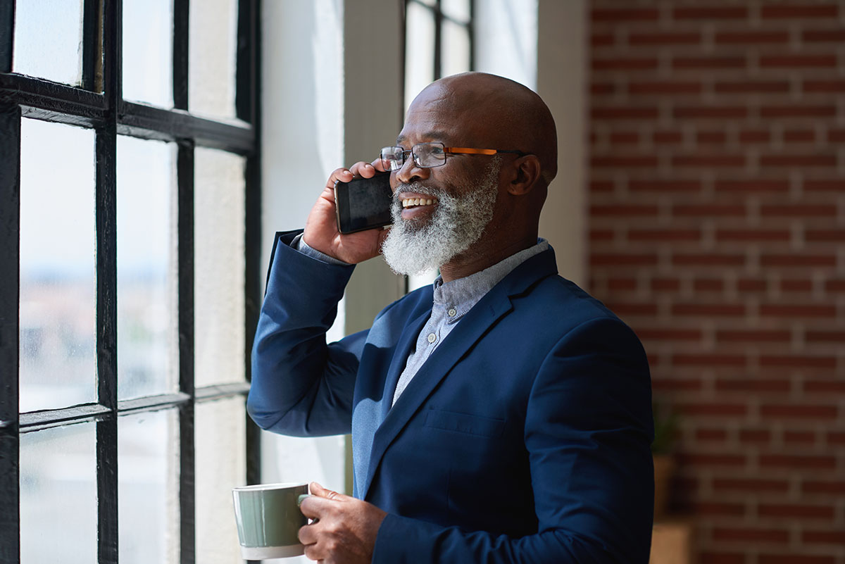 African american businessman using smartphone talking having phone call conversation in office looking out window